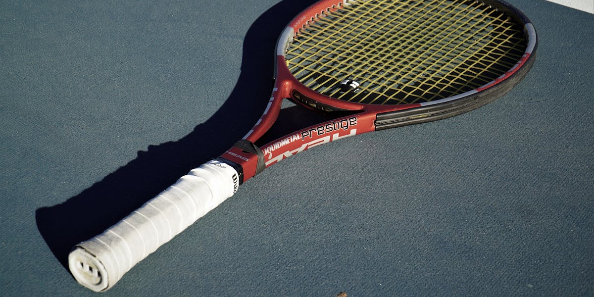 A high-quality tennis racket placed on a blue tennis court under sunlight.