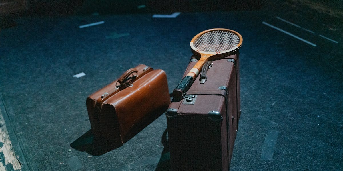 Classic leather bags and a tennis racket on a dark indoor surface, evoking vintage...