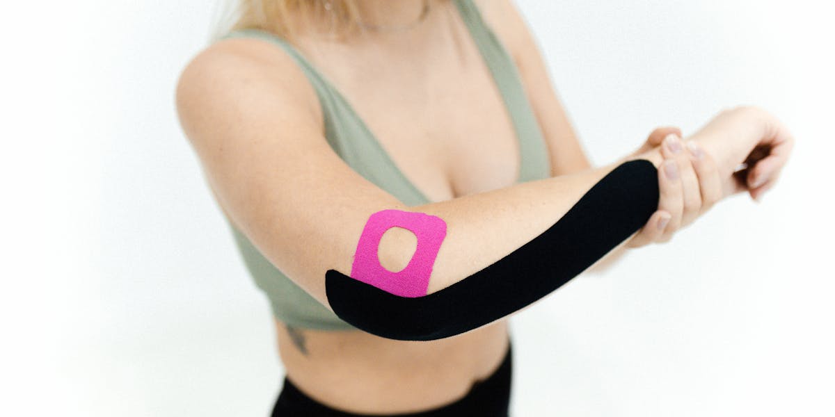 Close-up of a woman applying kinesio tape on her arm for therapeutic treatment on ...