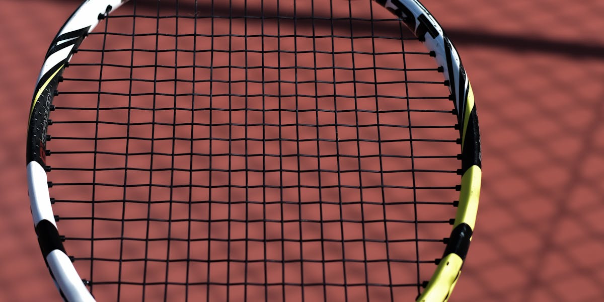 Close-up of a tennis racket on a clay court showing string pattern and brand det