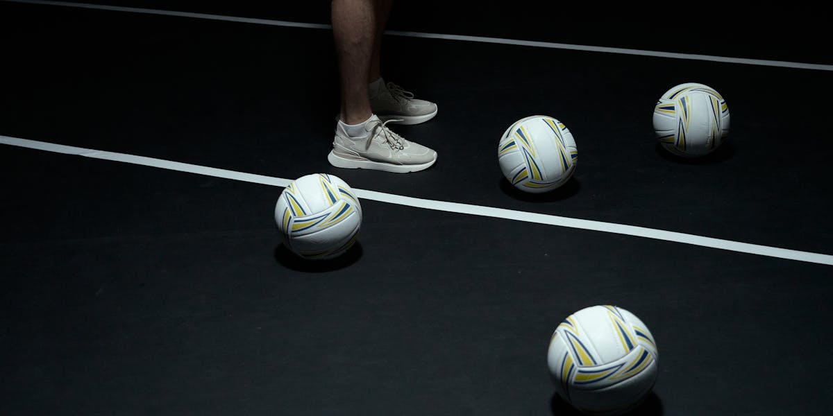 Person in sneakers with volleyballs on indoor court.